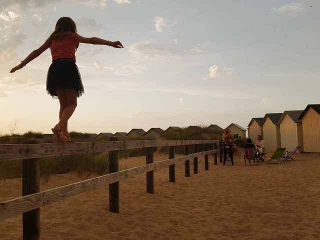 Fillette en équilibre sur une barrière en bois et groupes d'amis prenant l'apéritif à la plage